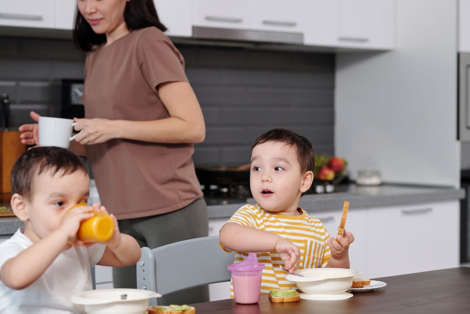 Mother feeding two young children breakfast together in the kitchen
