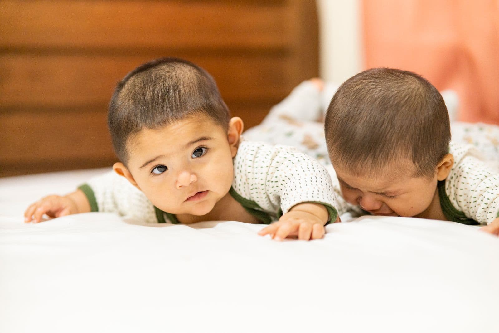 Twin babies during tummy time play on a bed